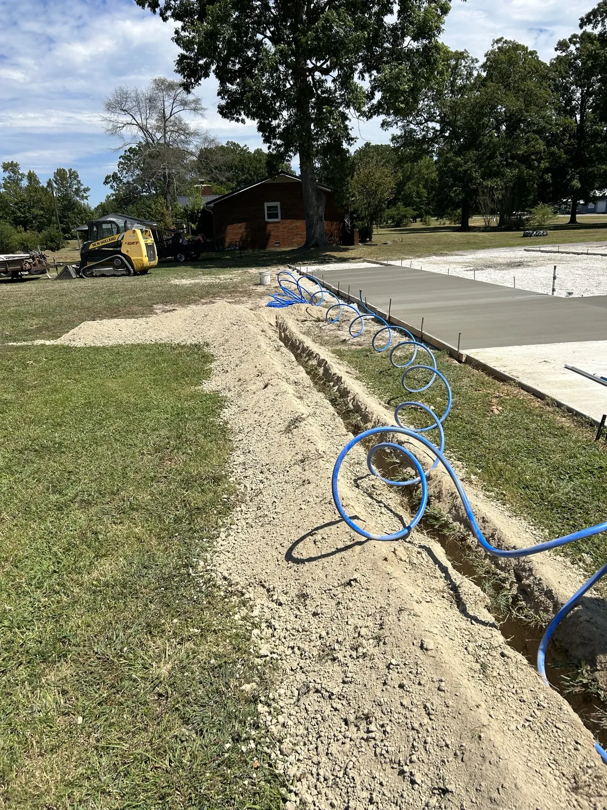 Blue water line laid in a trench beside a concrete slab